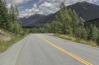 a long straight road with a yellow line next to a tree covered mountain valley and blue skies