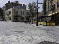 a cobblestone road in front of old buildings and businesses with a yellow cab and umbrella stand