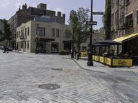 a cobblestone road in front of old buildings and businesses with a yellow cab and umbrella stand