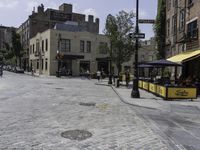 a cobblestone road in front of old buildings and businesses with a yellow cab and umbrella stand