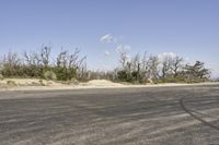 a view along a dirt road of an empty field and mountains in the distance of the scene