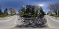 a 360 - angle view of a long asphalt road near trees, with the sun reflecting off the shadows of the street