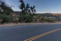 a person riding on the back of a motorcycle down an empty road next to mountains