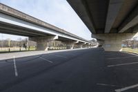 a large bridge going over a parking lot next to an empty road for cars to drive across