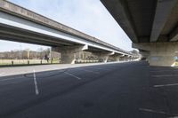 a large bridge going over a parking lot next to an empty road for cars to drive across