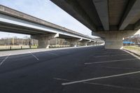 a large bridge going over a parking lot next to an empty road for cars to drive across