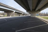 a large bridge going over a parking lot next to an empty road for cars to drive across