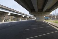 a large bridge going over a parking lot next to an empty road for cars to drive across