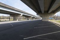 a large bridge going over a parking lot next to an empty road for cars to drive across