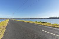 the empty country road leads across a beautiful lake area on a sunny day with blue skies and mountains in the background