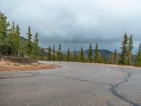 there is a black sign that is on a road with mountains in the background, on top of a hill near trees