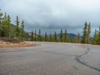 there is a black sign that is on a road with mountains in the background, on top of a hill near trees