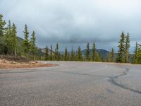 there is a black sign that is on a road with mountains in the background, on top of a hill near trees