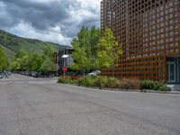 street corner with tree on the corner of the corner and a building behind it that is surrounded by multiple windows and a perforated brown lattice