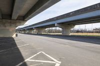 a view underneath an overpass from a parking area below a bridge as people ride on bicycles