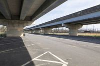 a view underneath an overpass from a parking area below a bridge as people ride on bicycles