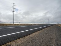 there is a asphalt road in the country side, and power poles behind it are very tall and bare and empty