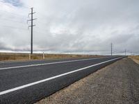 there is a asphalt road in the country side, and power poles behind it are very tall and bare and empty