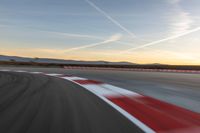 a photo of a dirt race track with sun setting in the distance of the track