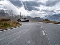 the empty highway is near mountains under a cloudy sky above a small cabin in a valley