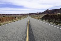 the road that is paved through the desert plain is empty and a yellow line goes up