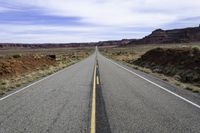 the road that is paved through the desert plain is empty and a yellow line goes up