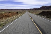 the road that is paved through the desert plain is empty and a yellow line goes up