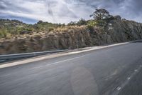 a motorcycle rides on the road in front of a cliff and trees along a rocky cliff