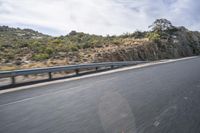 a motorcycle rides on the road in front of a cliff and trees along a rocky cliff