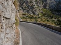 a person on a motor bike on a long winding road near some rock walls and grass