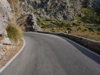 a person on a motor bike on a long winding road near some rock walls and grass