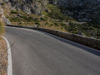 a person on a motor bike on a long winding road near some rock walls and grass