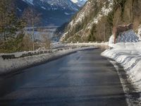 a paved road winds around the mountains next to a mountain road that has snow on it