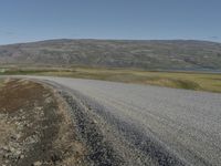 an asphalt road with gravel and rocks under a partly sunny blue sky on a hill side