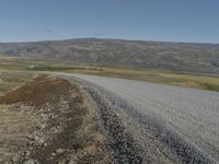 an asphalt road with gravel and rocks under a partly sunny blue sky on a hill side