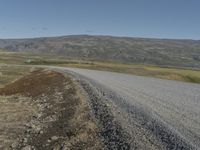 an asphalt road with gravel and rocks under a partly sunny blue sky on a hill side