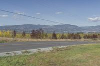 a view of the mountains with a street and grass near the side of it on a sunny day