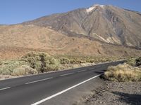 two people on motorcycles are riding down the road to go around an volcano, with mountains in the background