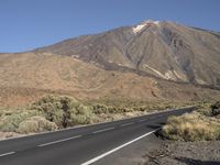 two people on motorcycles are riding down the road to go around an volcano, with mountains in the background