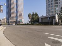 an empty road in front of tall buildings near a street with trees on one side and cars on the other