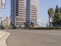 an empty road in front of tall buildings near a street with trees on one side and cars on the other