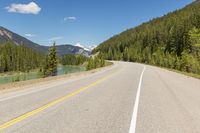 the highway is narrow and winding into a lake and mountains with trees in the distance