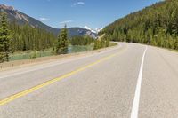 the highway is narrow and winding into a lake and mountains with trees in the distance