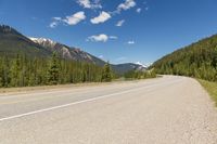 the highway is narrow and winding into a lake and mountains with trees in the distance