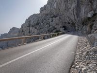 a long road near a mountain with a tunnel coming out into the valley, along side a large rock wall