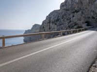 a long road near a mountain with a tunnel coming out into the valley, along side a large rock wall