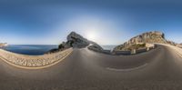 a curved asphalt road is in front of some mountains, some rocks and a ocean