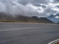 an asphalt road next to a mountain in the clouds with a motorcycle and mountain range