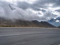 an asphalt road next to a mountain in the clouds with a motorcycle and mountain range