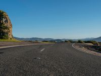 a empty road leading towards mountains in the distance with trees on one side and blue skies in the other